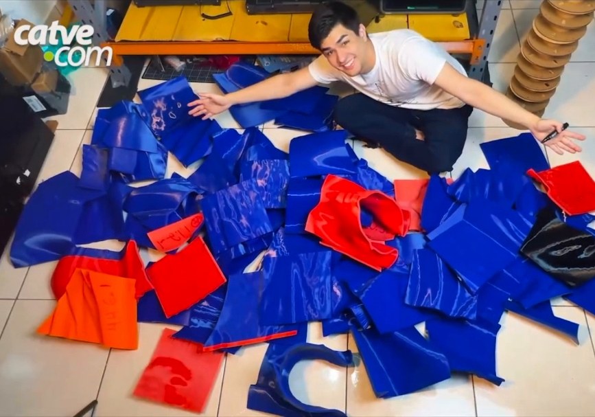 Young man sitting on the floor among dozens of blue and red 3D-printed parts