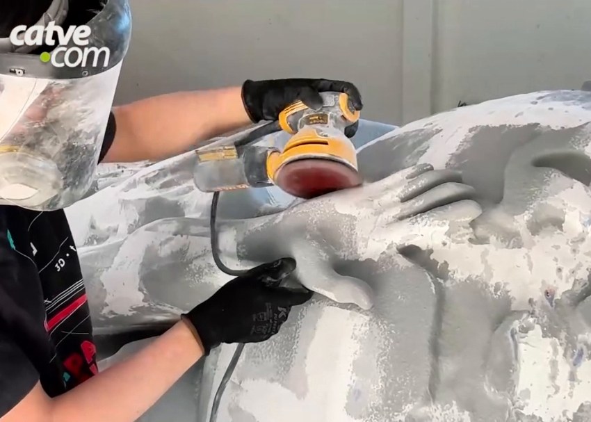 Sander on the filler-coated surface of the trophy, next to a sculpted hand