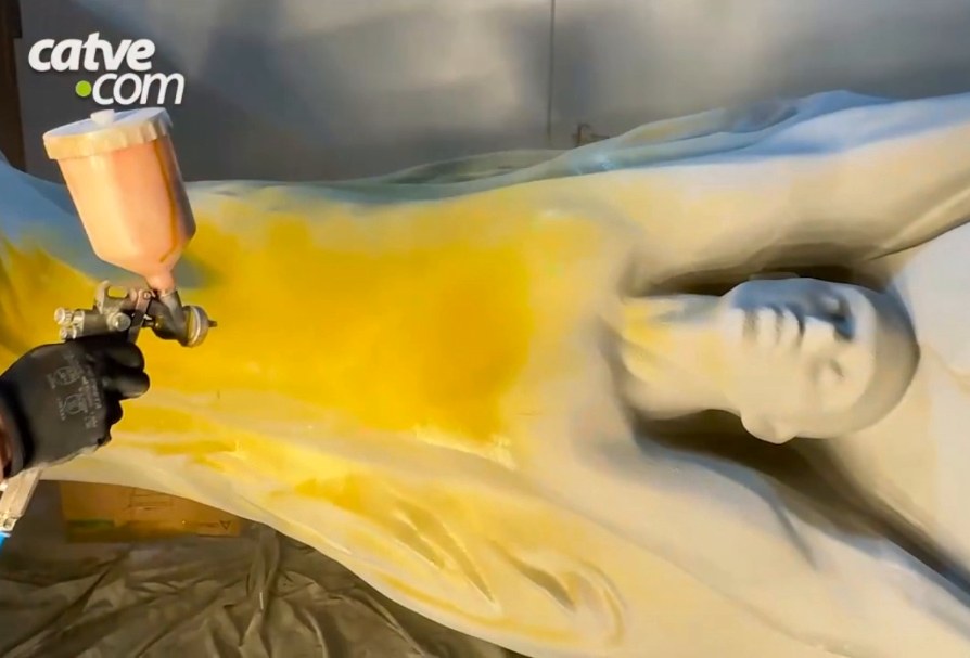 Spray gun applying yellow paint to the sculpted figure of the trophy
