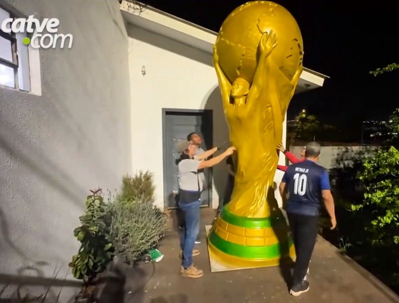 The giant golden trophy standing in front of the house at night, surrounded by the team