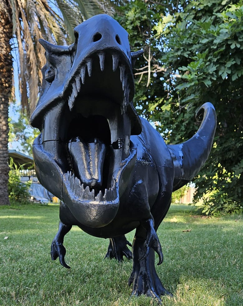Black T. rex seen from the front, jaws open, in a garden